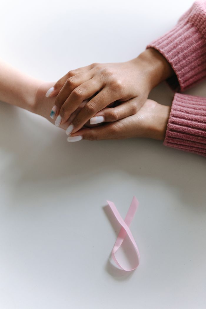 approach-img Close-up of two hands holding with a pink ribbon symbolizing cancer awareness.
