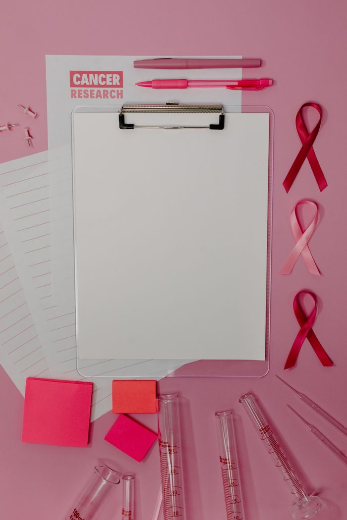 Clipboard with pink ribbons and cancer research papers on a pink background.