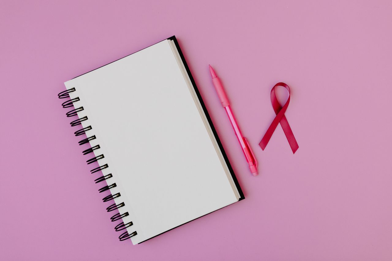 Pink ribbon and notebook on a pink background, symbolizing breast cancer awareness and advocacy.